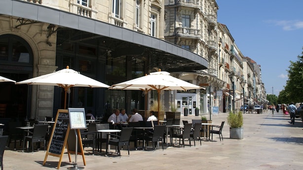 Ein Straßencafé mit Tischen, Stühlen und einer Speisekarte, im Hintergrund ein Gebäude im klassischen Stil.