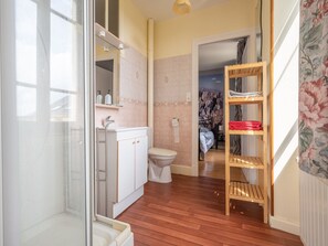 Une salle de bain avec une douche, des toilettes et un lavabo. On y trouve une étagère en bois où sont posées des serviettes.