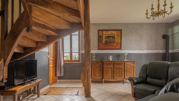 Un salón amplio con escalera de madera, un sofá de cuero, un televisor sobre un mueble de madera y una araña.