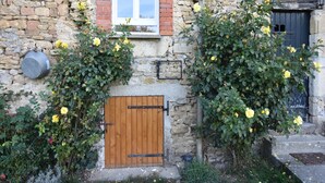 Un edificio de piedra con puerta de madera, una ventana y un pequeño balcón con flores amarillas.