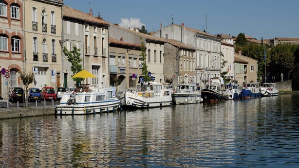 Un canal bordé de bateaux à quai, entouré d’immeubles dotés de balcons et de fenêtres.