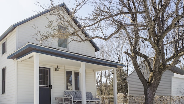 A two-story white house with a porch, a covered front door, and a small outdoor seating area.