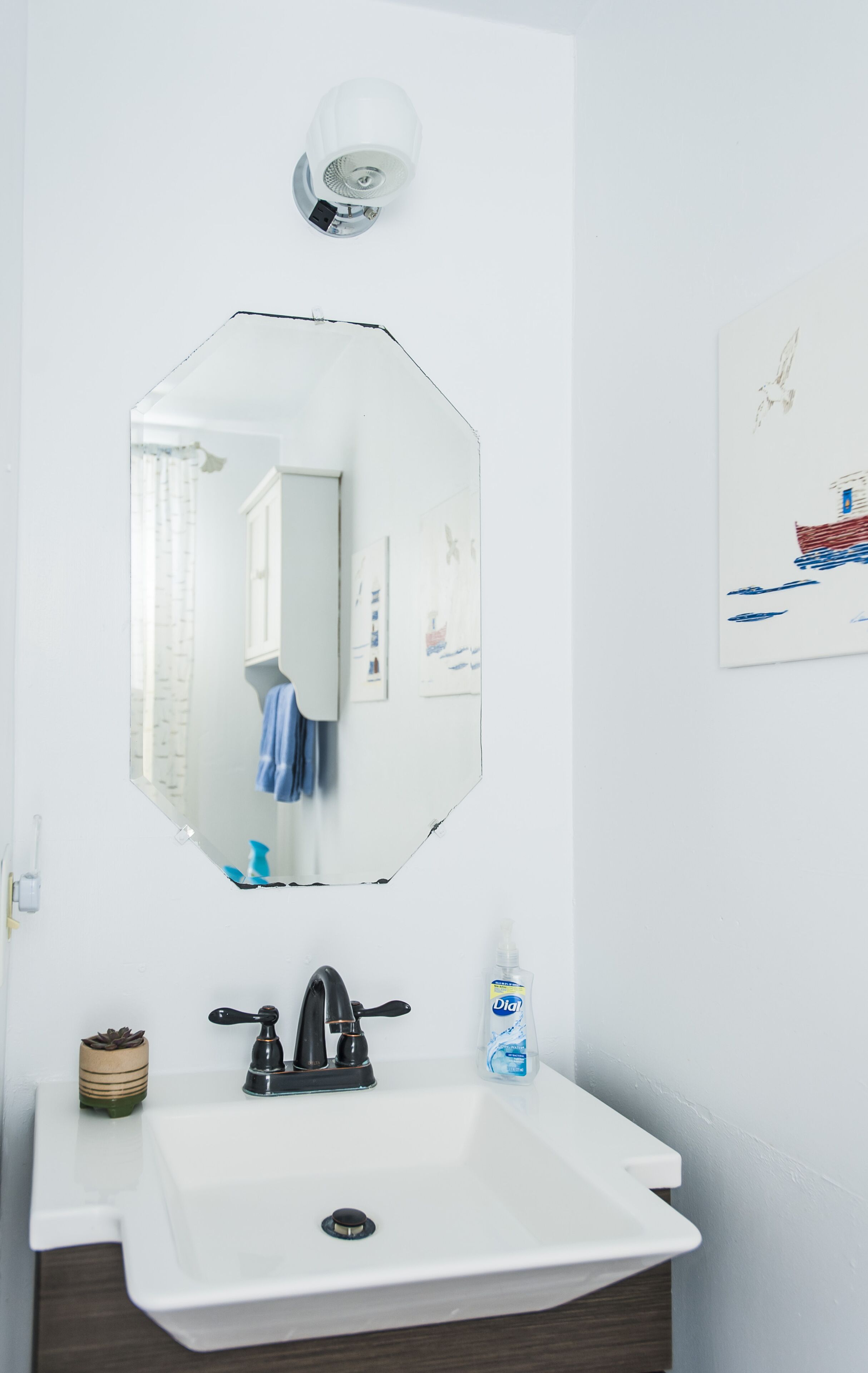 A bathroom with a white sink, a black faucet, a mirror, a light fixture, and a small potted plant.