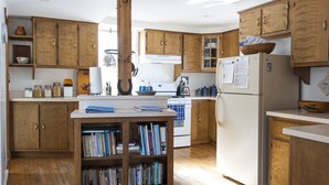 A kitchen with wooden cabinets, a central island with books, a refrigerator, and a stove.