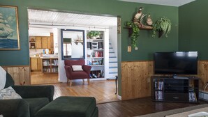 A cozy living room with a red armchair, a green ottoman, and a television on a wooden stand.