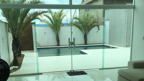 Una sala de estar moderna con un ventanal que da a una zona de piscina, un sofá blanco y una alfombra verde.