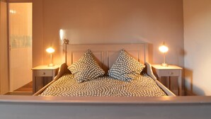 Un dormitorio con una cama, dos mesitas de noche, dos lámparas y una puerta que da a otra habitación.
