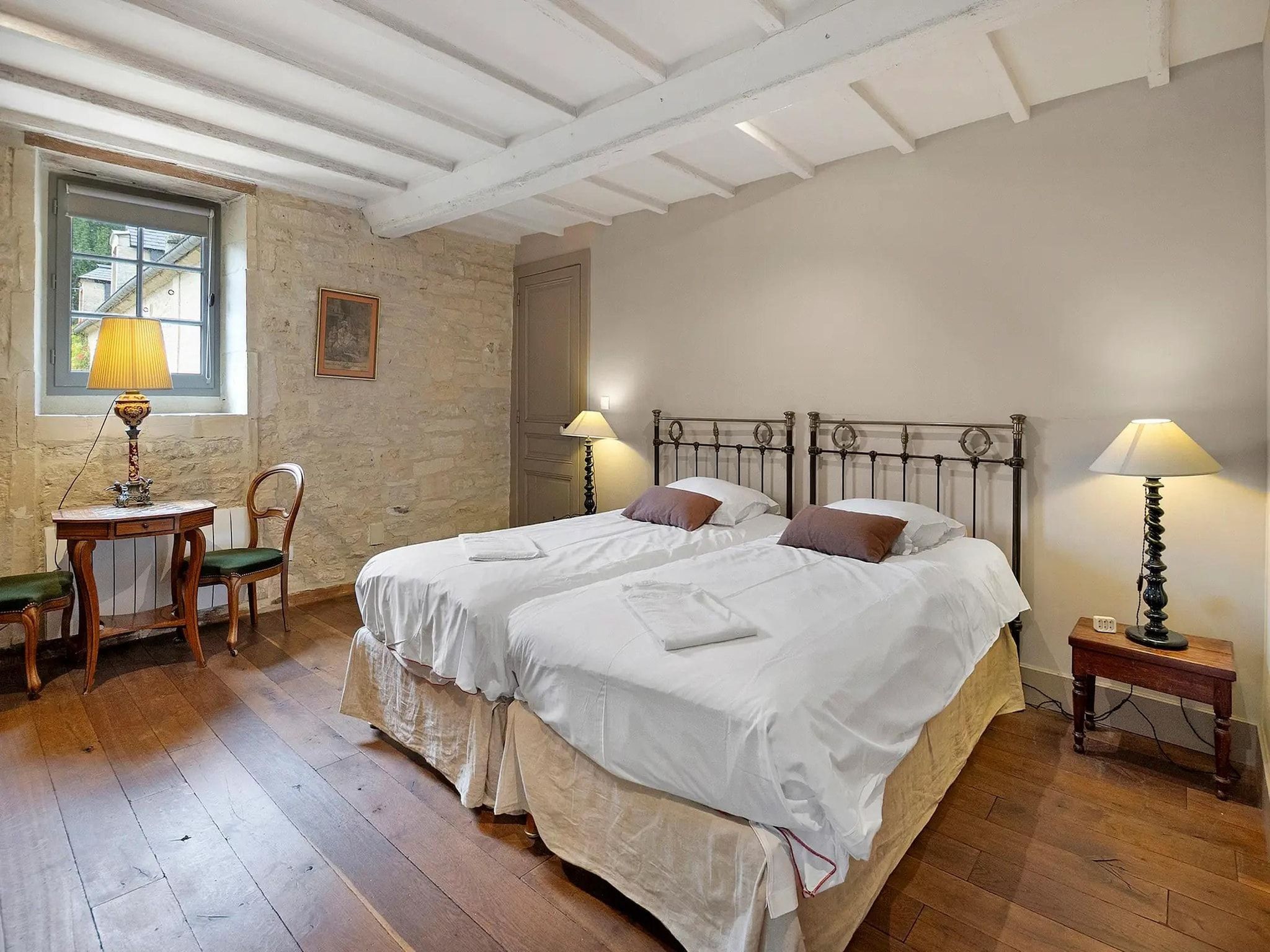 Une chambre à coucher avec un lit double, deux tables de chevet avec des lampes, un petit bureau en bois avec une chaise et une fenêtre donnant sur un beau paysage.