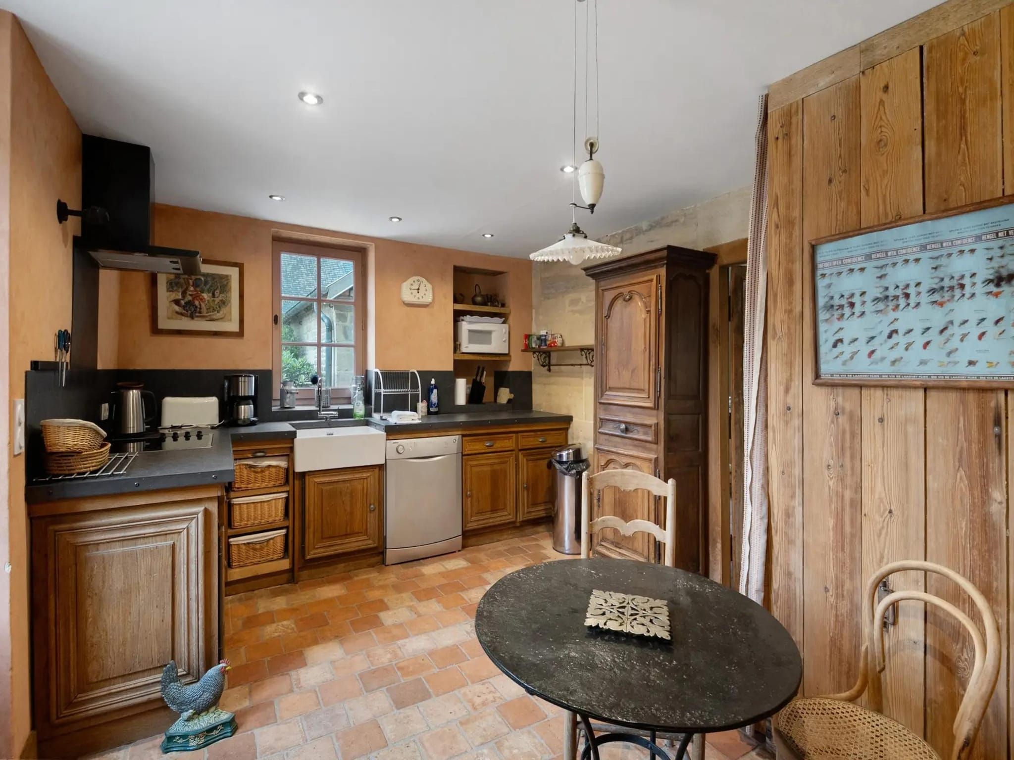 Une cuisine compacte avec des meubles en bois, un plan de travail noir, un évier, un lave-vaisselle et un coin repas comprenant une table et des chaises.