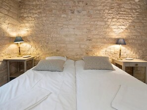 Une chambre avec un mur en pierre, deux lits avec du linge de lit blanc et deux tables de chevet avec des lampes.