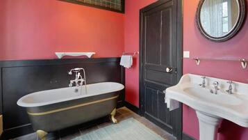 Une salle de bain avec une baignoire sur pieds, un lavabo, une porte et un miroir au mur.