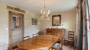 Une salle à manger avec une table en bois, des chaises, un lustre, un miroir et des rideaux.