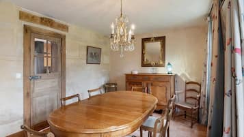 Une salle à manger avec une table en bois, des chaises, un lustre, un miroir et des rideaux.