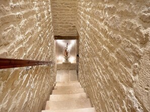 Un escalier en pierre mène à une statue située dans une pièce aux murs à texture.