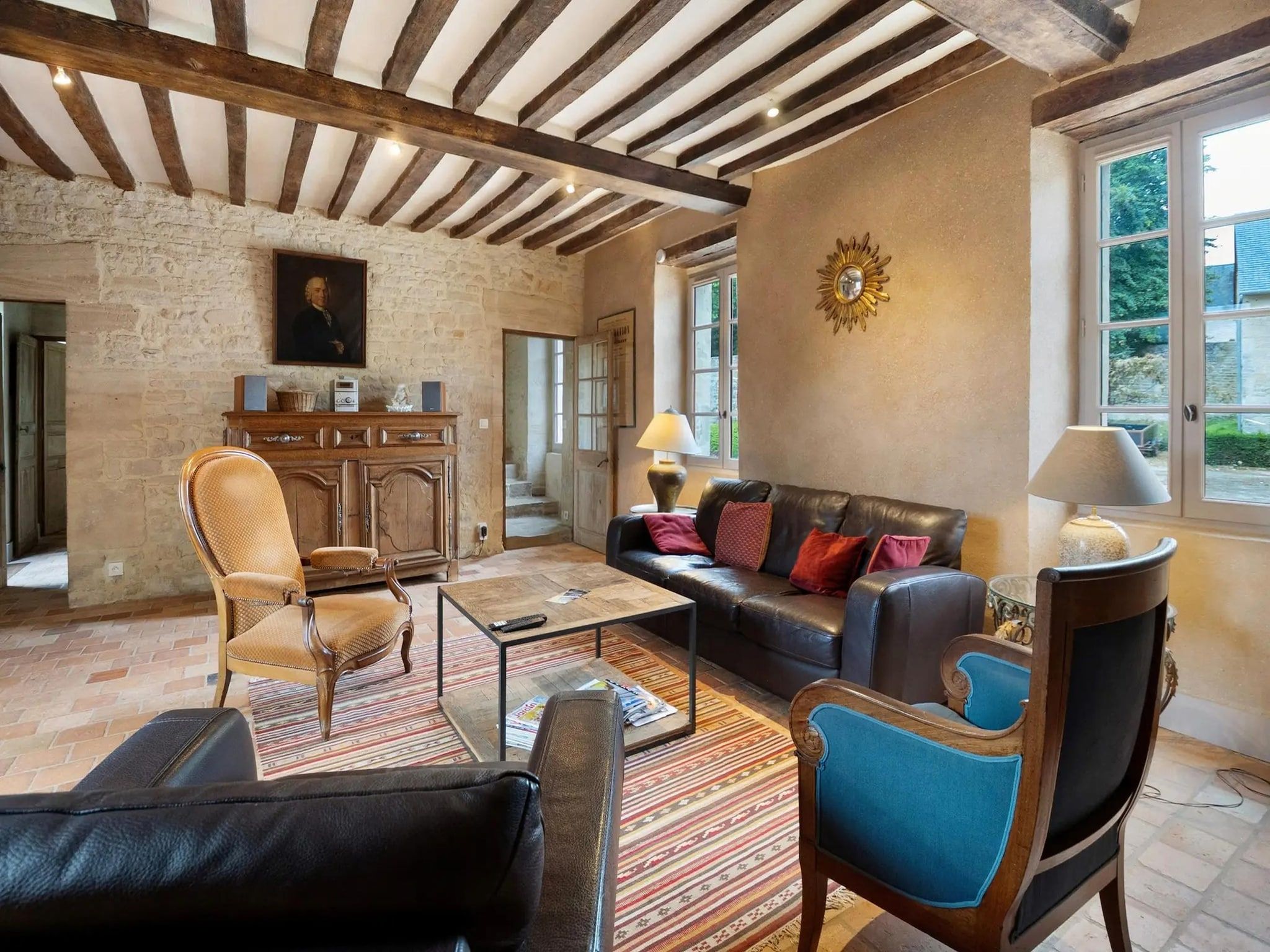 Un salon spacieux avec un mur en pierre, des poutres apparentes, un canapé en cuir et une grande fenêtre.