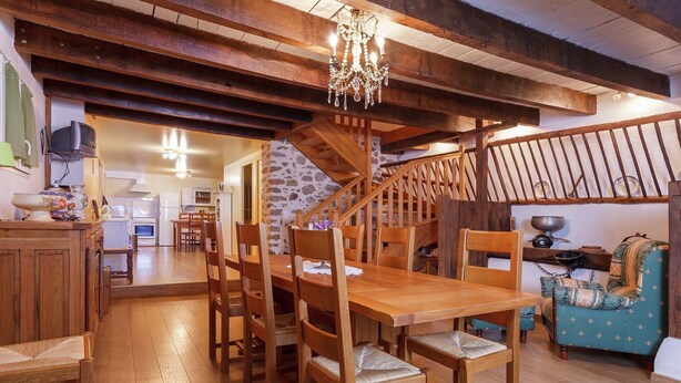 Una mesa de madera con sillas, una escalera y una zona de estar acogedora con un sofá estampado.