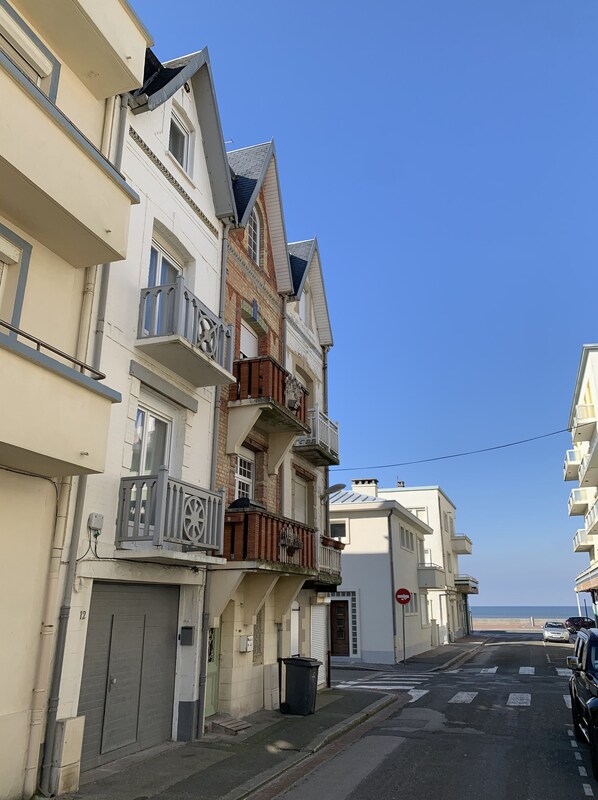 Een meerhoog gebouw met balkons, een hekwerk en een helder uitzicht op de straat en het strand op de achtergrond.