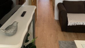 Ein Flur mit Fernseher, Fernbedienung und einem dekorativen Gegenstand auf einer Ablage, der zu einem Küchenbereich mit Mikrowelle und Schränken führt.