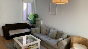 Ein Wohnzimmer mit braunem Sofa, einem beigen Sofa, einem Glastisch und einem Korbstuhl.