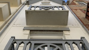 Ein flachdaches Gebäude mit weißer Fassade, einem zentralen Fenster und einem dekorativen Metallgeländer.