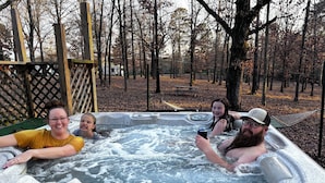 Un jacuzzi con cuatro personas, rodeado por una terraza de madera y árboles.