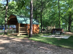 Un chalet rustique avec une véranda, entouré d’arbres, et une table de pique-nique à proximité.