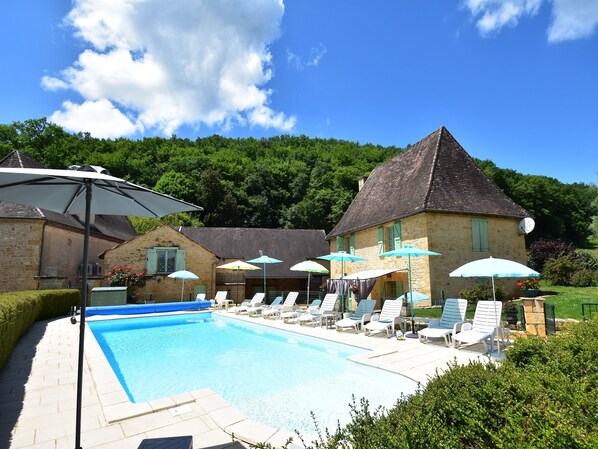 A swimming pool with lounge chairs and umbrellas, surrounded by stone buildings and greenery.