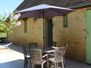 A stone building with a table and chairs under a large umbrella.