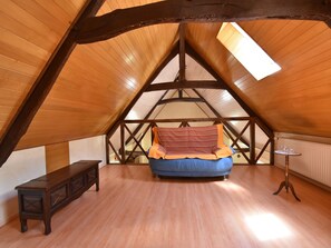 A bedroom with a sloped ceiling, wooden beams, a bed with a striped blanket, a small table, and a bench.