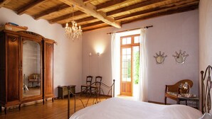 A room with a wooden ceiling, a large bed, a wooden wardrobe, a chandelier, and a window with curtains. - Hilltop Mansion with Pool (Sigoulès)
