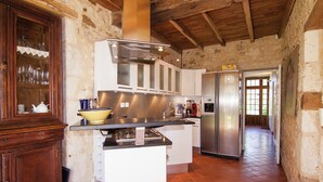 A rustic kitchen with a central island, wooden cabinets, and a stainless steel refrigerator. - Hilltop Mansion with Pool (Sigoulès)