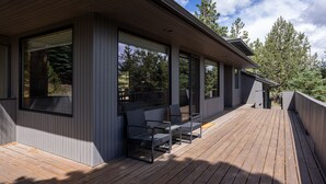A modern house with a wooden deck, large windows, and outdoor seating.