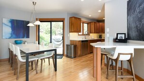 A modern kitchen with wooden cabinets, a white countertop, and a dining area with a table and chairs.