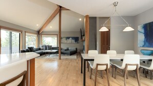 A spacious living area with a dining table, white chairs, and a large window.