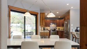A modern kitchen with wooden cabinets, a stainless steel refrigerator, and a dining area with a marble table and white chairs.