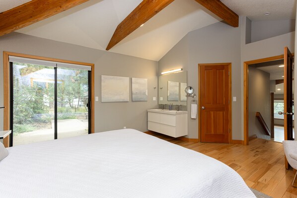 A bedroom with a large bed, a wooden ceiling, a bathroom with a vanity, and a sliding glass door to a balcony.