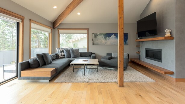 A modern living room with a sectional sofa, a coffee table, a fireplace, and a TV mounted on a wooden shelf.