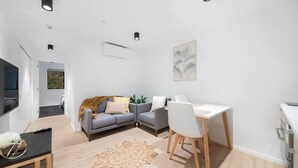 A modern living room with a grey sofa, a white desk, and a wooden floor. - 1 Bedroom Modern Apartment in Queenstown (Queenstown)