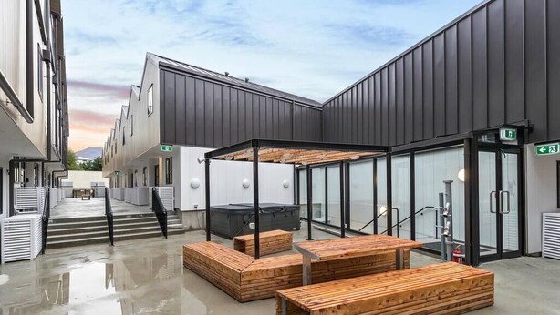 A modern building with a glass entrance, wooden benches, and a clear sky. - 1 Bedroom Modern Apartment in Queenstown (Queenstown)