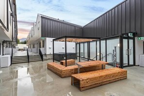 Un bâtiment moderne avec une entrée en verre, des bancs en bois et un ciel dégagé.