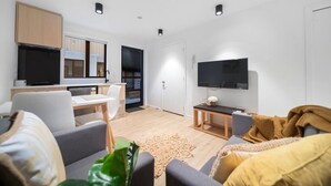 A modern living room with a sofa, a coffee table, and a TV. There is a kitchen area with cabinets and a dining table. - 1 Bedroom Modern Apartment in Queenstown (Queenstown)
