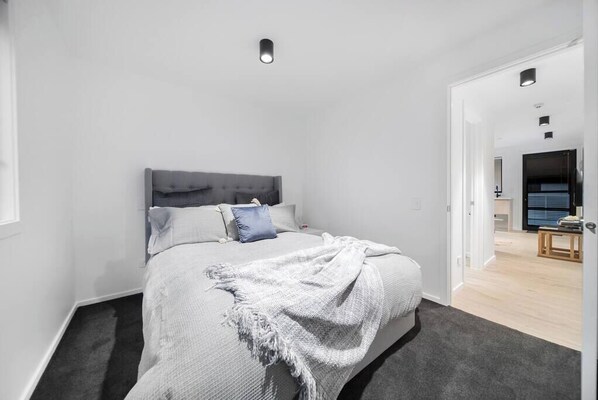 Une chambre moderne avec une tête de lit grise, un couvre-lit blanc et un coussin bleu.