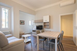 A compact living space with a dining table, chairs, a sofa, a TV, and built-in shelving.