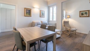 Un comedor con una mesa y sillas de madera, un sofá, una lámpara y cuadros en las paredes.