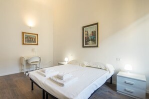 A hotel room with a bed, bedside tables, a desk, and two paintings on the walls.