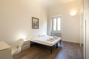 Una camera da letto con un letto, un comodino, una sedia e una finestra con termosifone.