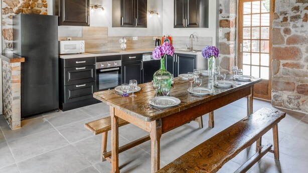 A rustic kitchen with stone walls, wooden beams, and a wooden dining table set with plates and glasses. - Beautiful holiday home with pool in Teillots (Teillots)