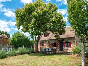 A stone house with a tiled roof, a dining area with outdoor furniture, and a large tree in the foreground. - Tranquil holiday home with private pool (Teillots)