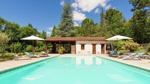 Un espace piscine comprenant un bâtiment, des chaises longues et des parasols.