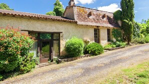 Une maison de campagne en pierre, avec un toit en tuiles, une porte en bois et une allée gravillonnée.